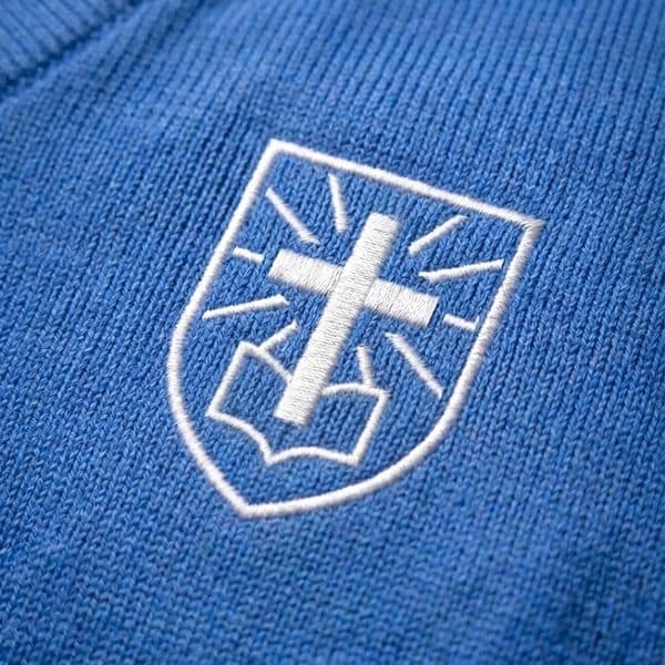 El escudo del colegio bordado en azul sobre la prenda